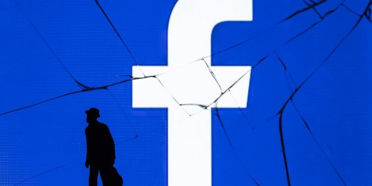 This photograph taken on May 16, 2018, shows a figurine standing in front of the logo of social network Facebook on a cracked screen of a smartphone in Paris. / AFP PHOTO / JOEL SAGET