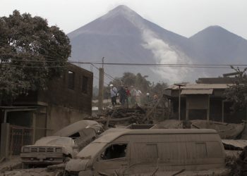 Rescue workers walk on rooftops in Escuintla, Guatemala, Monday, June 4, 2018, blanketed with heavy ash spewed by the Volcan de Fuego, or "Volcano of Fire," pictured in the background, left center. A fiery volcanic eruption in south-central Guatemala sent lava flowing into rural communities, killing at least 25 as rescuers struggled to reach people where homes and roads were charred and blanketed with ash. (AP Photo/Luis Soto)