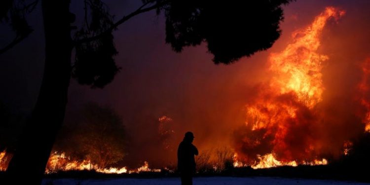 A man looks at the flames as a wildfire burns in the town of Rafina, near Athens. REUTERS/Costas Baltas