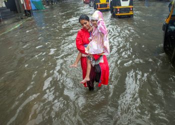 Thane: A woman, carrying a girl, wades through a waterlogged road during heavy rains, in Thane on Monday, July 9, 2018. (PTI Photo) (PTI7_9_2018_000039B)