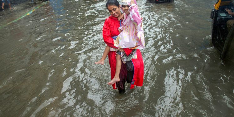 Thane: A woman, carrying a girl, wades through a waterlogged road during heavy rains, in Thane on Monday, July 9, 2018. (PTI Photo) (PTI7_9_2018_000039B)