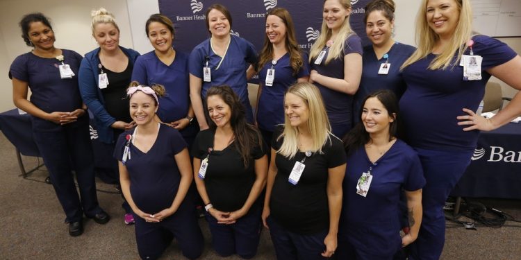 Most of the sixteen pregnant nurses who work together in the intensive care unit at Banner Desert Medical Center pose for a group photograph after attending a news conference where they all talked about being pregnant at the same time, with most of them due to give birth between October and January, Friday, Aug. 17, 2018, in Mesa, Ariz. (AP Photo/Ross D. Franklin)