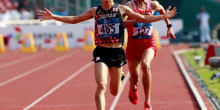 Japan’s Hiroto Inoue celebrates as he crosses the line to win the men’s marathon with Bahrain’s Elhassan Elabbassi trying to catch up 