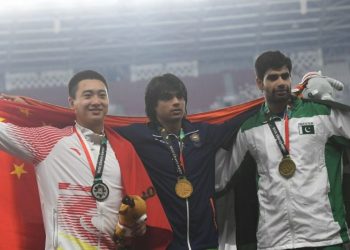 Neeraj Chopra (C) is flanked by China’s Liu Qizhen (L) and Pakistan’s Arshad Nadeem as the trio pose, with their respective flags and medals, for shutterbugs at Jakarta