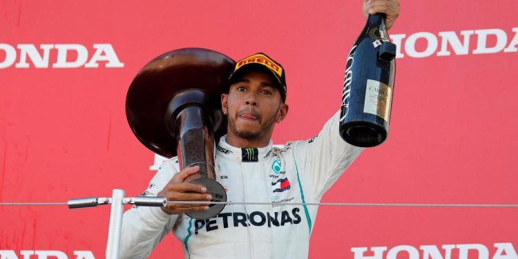 Lewis Hamilton, with the winner’s trophy on his shoulder, holds the champaign aloft while celebrating his victory at Suzuka, Sunday  