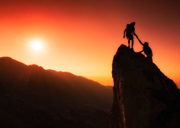 Team of climbers help to conquer the summit in teamwork in a fantastic mountain landscape at sunset