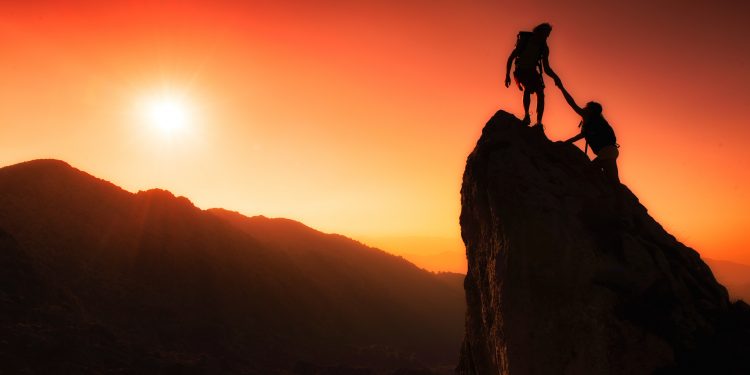 Team of climbers help to conquer the summit in teamwork in a fantastic mountain landscape at sunset