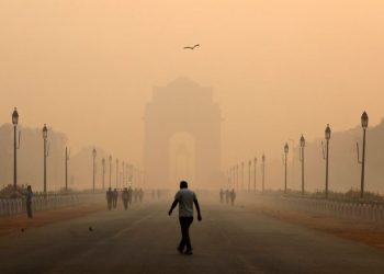 A man walks in front of the India Gate covered in smog.