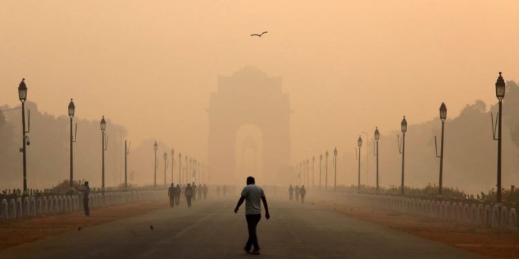 A man walks in front of the India Gate covered in smog.