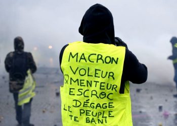 A demonstrator wearing a yellow jacket reading "Macron, thief, liar, crook, go away, the people banish you" near the Champs-Elysees avenue during a demonstration Saturday, Dec.1, 2018 in Paris.