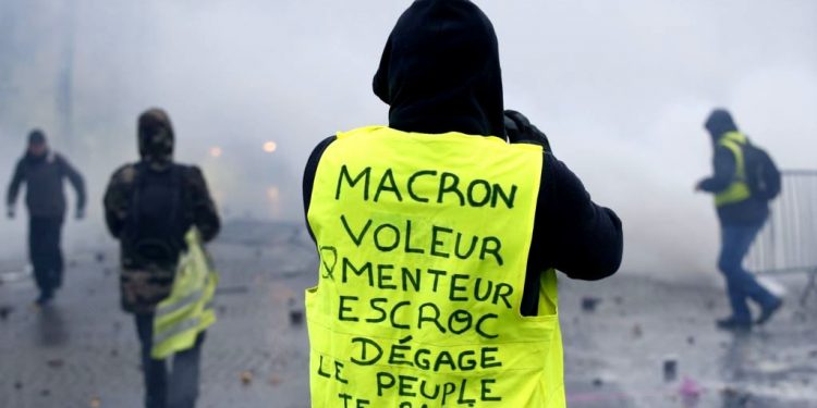A demonstrator wearing a yellow jacket reading "Macron, thief, liar, crook, go away, the people banish you" near the Champs-Elysees avenue during a demonstration Saturday, Dec.1, 2018 in Paris.