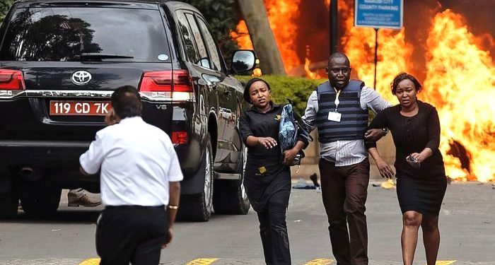 Security forces help civilians flee the scene as cars burn behind. (AP)