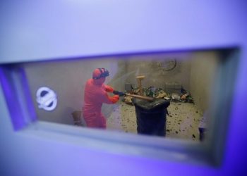 Customer Liu Chao, wearing protective gear, is seen through a window as he smashes bottles in an anger room in Beijing, China. REUTERS/Jason Lee