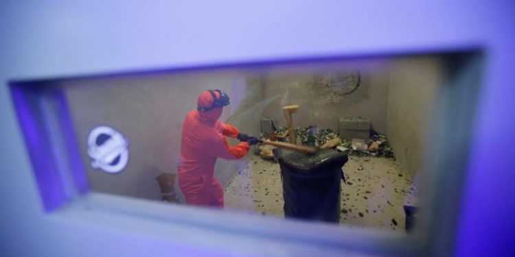 Customer Liu Chao, wearing protective gear, is seen through a window as he smashes bottles in an anger room in Beijing, China. REUTERS/Jason Lee