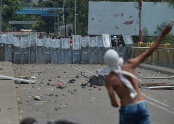 A demonstrator throws stones at Venezuelan national policemen standing guard at the Simon Bolivar international bridge, in Cucuta, Colombia (AFP)