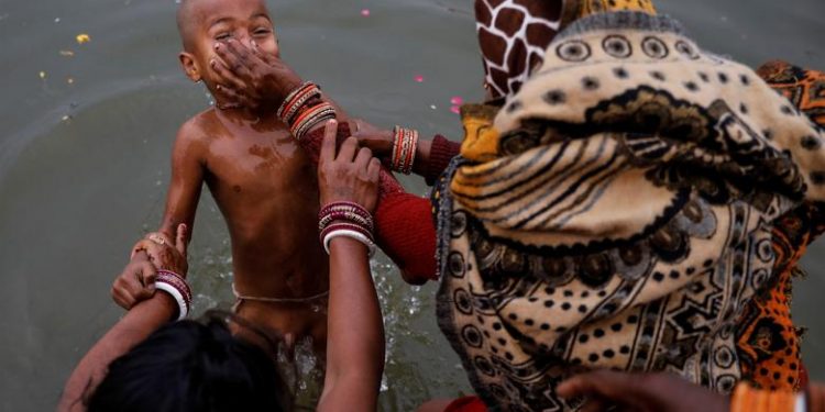 A woman holds the nose of her son as she dips him at Sangam, the confluence of the Ganges, Yamuna and Saraswati rivers, ahead of the "Kumbh Mela", or the Pitcher Festival, in Prayagraj, previously known as Allahabad, India, January 13, 2019. (REUTERS/Danish Siddiqui)