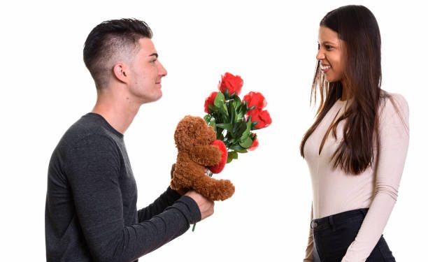 Young happy couple smiling and in love with man giving red roses and teddy bear horizontal shot