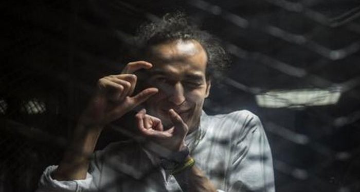 Egyptian photographer Mahmoud Abu Zeid, known as Shawkan, gestures from inside a soundproof glass dock during his trial in Cairo on August 9, 2016. (AFP)