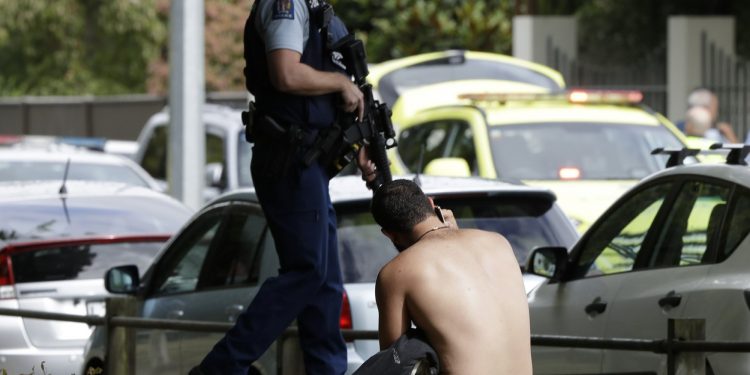 A man rests on the ground as he speaks on his mobile phone across the road from mosque in central Christchurch, New Zealand, Friday, March 15, 2019. A witness says a number of people have been killed in a mass shooting at a mosque in the New Zealand city of Christchurch; police urge people to stay indoors. (AP Photo/Mark Baker)