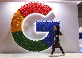 In this Monday, Nov. 5, 2018, photo, a woman carries a fire extinguisher past the logo for Google at the China International Import Expo in Shanghai. Internet traffic hijacking disrupted several Google services Monday, Nov. 12, 2018, including search and cloud-hosting services. (AP Photo/Ng Han Guan)