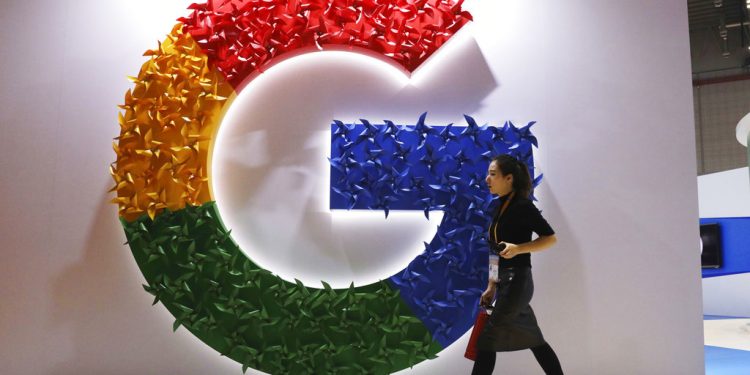 In this Monday, Nov. 5, 2018, photo, a woman carries a fire extinguisher past the logo for Google at the China International Import Expo in Shanghai. Internet traffic hijacking disrupted several Google services Monday, Nov. 12, 2018, including search and cloud-hosting services. (AP Photo/Ng Han Guan)