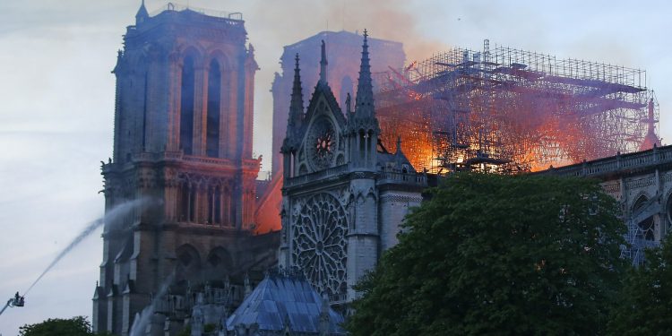 A firefighter tackles the blaze as flames and smoke rise from Notre Dame cathedral as it burns in Paris, Monday, April 15, 2019. Massive plumes of yellow brown smoke is filling the air above Notre Dame Cathedral and ash is falling on tourists and others around the island that marks the center of Paris. (AP Photo/Michel Euler)