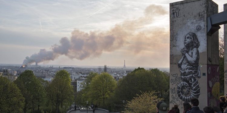 People watch Notre Dame cathedral burning in Paris, Monday, April 15, 2019. Massive plumes of yellow brown smoke is filling the air above Notre Dame Cathedral and ash is falling on tourists and others around the island that marks the center of Paris. (AP Photo/Rafael Yaghobzadeh)