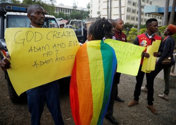 An LGBT activist walks past anti-gay rights protesters holding placards, after a ruling by Kenya's high court to upheld a law banning gay sex, outside the Milimani high Court in Nairobi