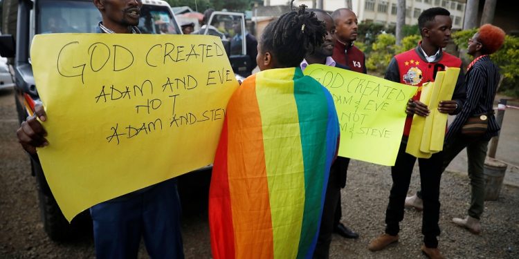 An LGBT activist walks past anti-gay rights protesters holding placards, after a ruling by Kenya's high court to upheld a law banning gay sex, outside the Milimani high Court in Nairobi