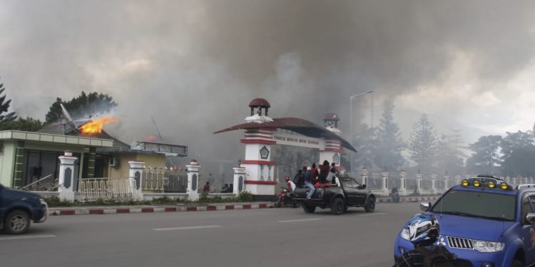 People drive past a blazing government building in Wamena, Monday