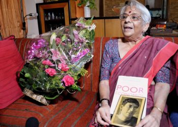 Nirmala Banerjee, mother of Indian-American economist Abhijit Banerjee, poses with her son's picture as flower bouquets arrive