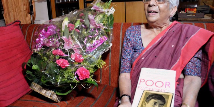 Nirmala Banerjee, mother of Indian-American economist Abhijit Banerjee, poses with her son's picture as flower bouquets arrive