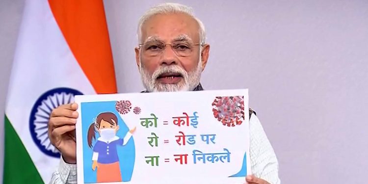 Prime Minister Narendra Modi holds a banner addresses the nation on the coronavirus pandemic, Tuesday