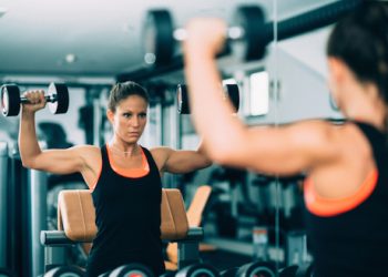 Young woman doing shoulder exercise in the gym with dumbbell