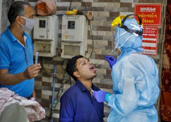 A lab technician wearing protective suit collects swab from a man for COVID-19 test in Ahmedabad