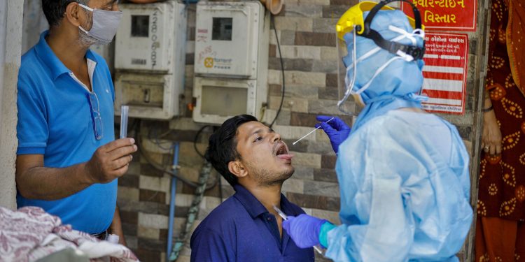 A lab technician wearing protective suit collects swab from a man for COVID-19 test in Ahmedabad