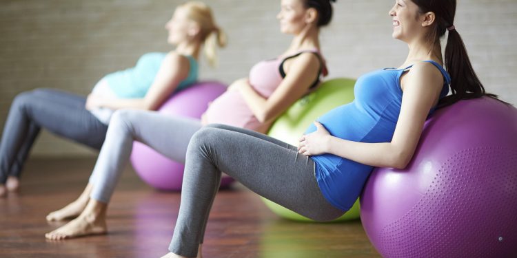 Several pregnant women exercising with ball in gym