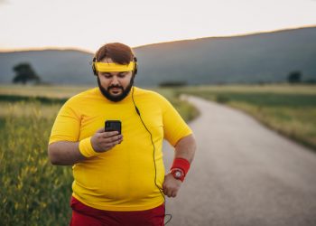 One man, young overweight man break after jogging, listening music on headphones, using smart phone.