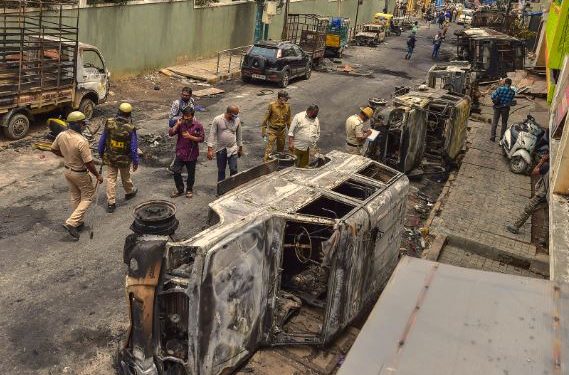 Bengaluru: Police and residents walk past charred remains of vehicles vandalised by a mob over a social media post, allegedly by a relative of a Congress MLA, in Bengaluru, Wednesday, Aug. 12, 2020. (PTI)