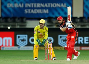 Virat Kohli drives through the cover region as CSK captain MS Dhoni looks on