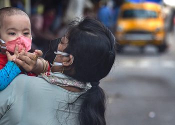 A woman adjusts the protective face mask of her child, at a deserted road during the ongoing COVID-induced lockdown in Kolkata (File | PTI)