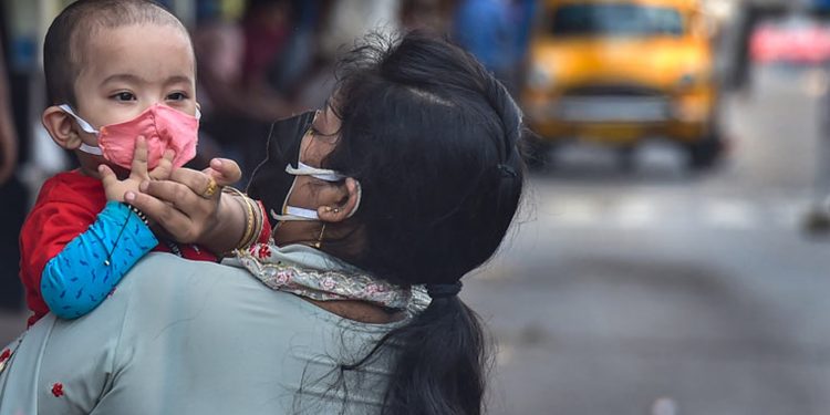 A woman adjusts the protective face mask of her child, at a deserted road during the ongoing COVID-induced lockdown in Kolkata (File | PTI)