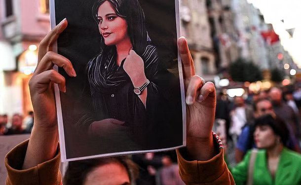 A protester holds up a portrait of Mahsa Amini. (Source: Wikimedia Commons)