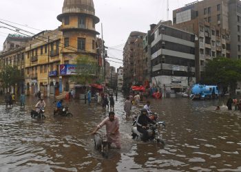 TOPSHOT - People wade across a flooded street after heavy monsoon rainfall in Karachi on July 25, 2022. (Photo by Asif HASSAN / AFP) (Photo by ASIF HASSAN/AFP via Getty Images)